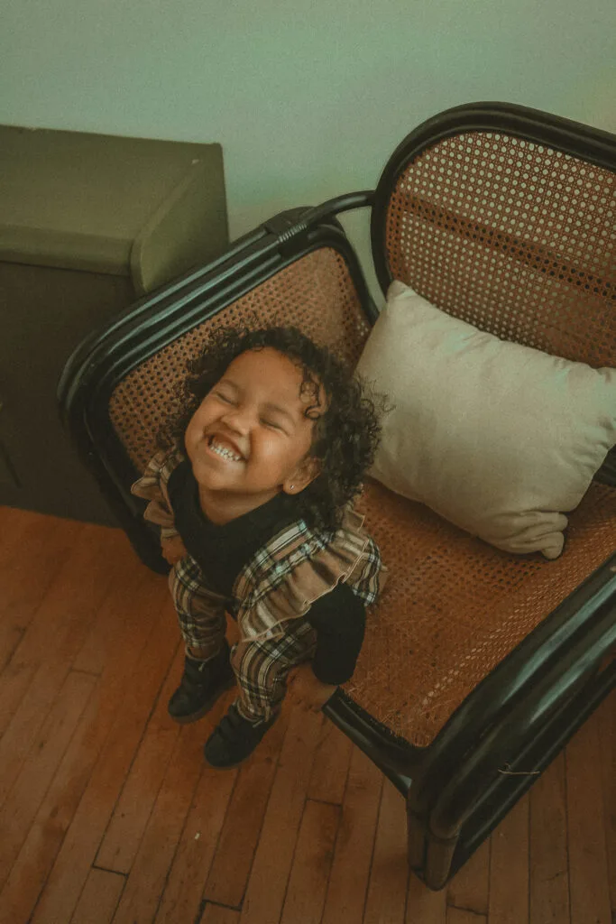 Joyful child laughing in cane chair during studio family photography session in East Hampton Connecticut