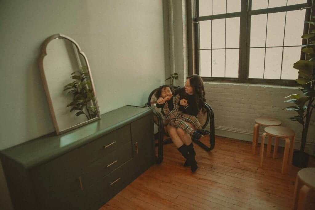 Mother laughing with young child in cane chair during natural light indoor family session in Connecticut
