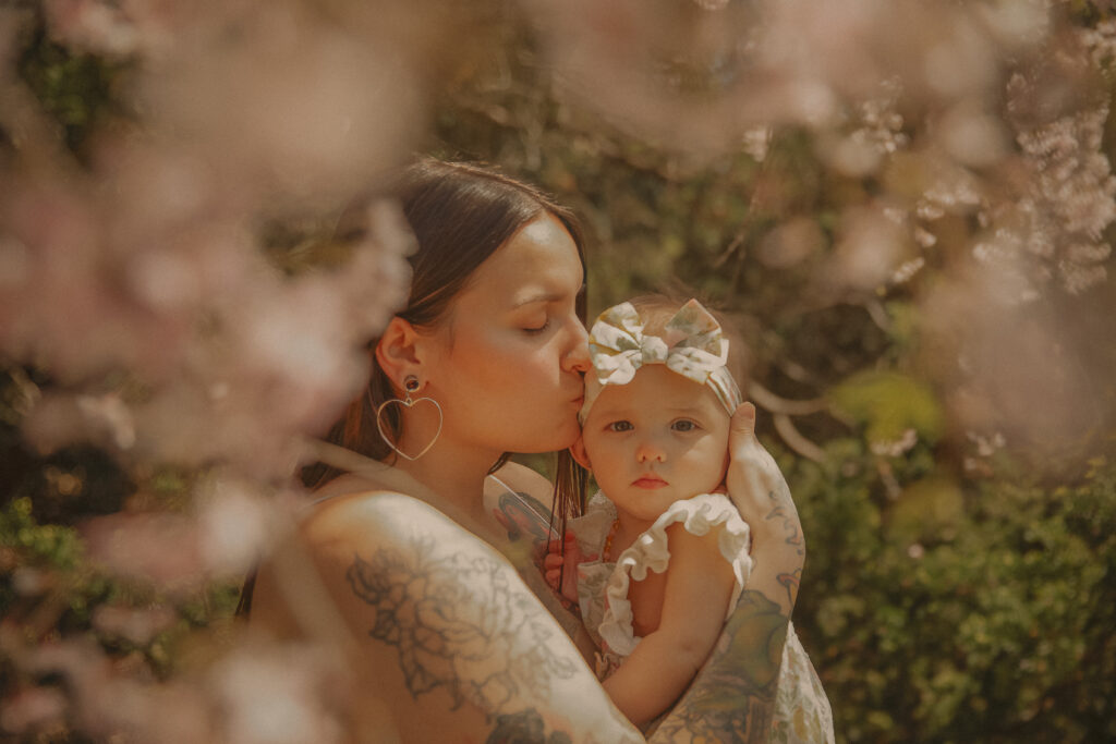 Mother kissing baby surrounded by spring blossoms during motherhood session in West Hartford Connecticut