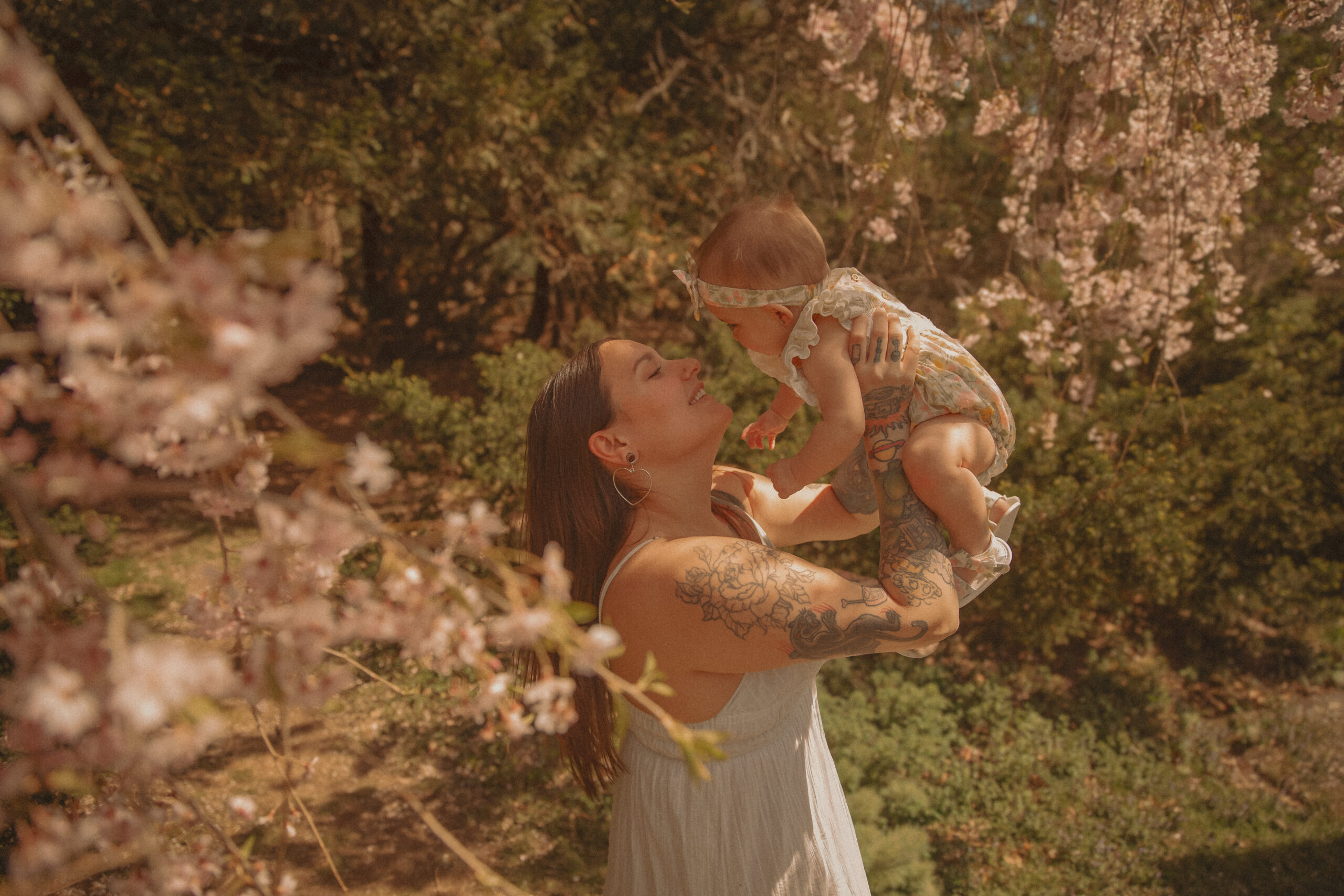 Mother lifting baby in blooming spring trees during outdoor motherhood photography session in Connecticut