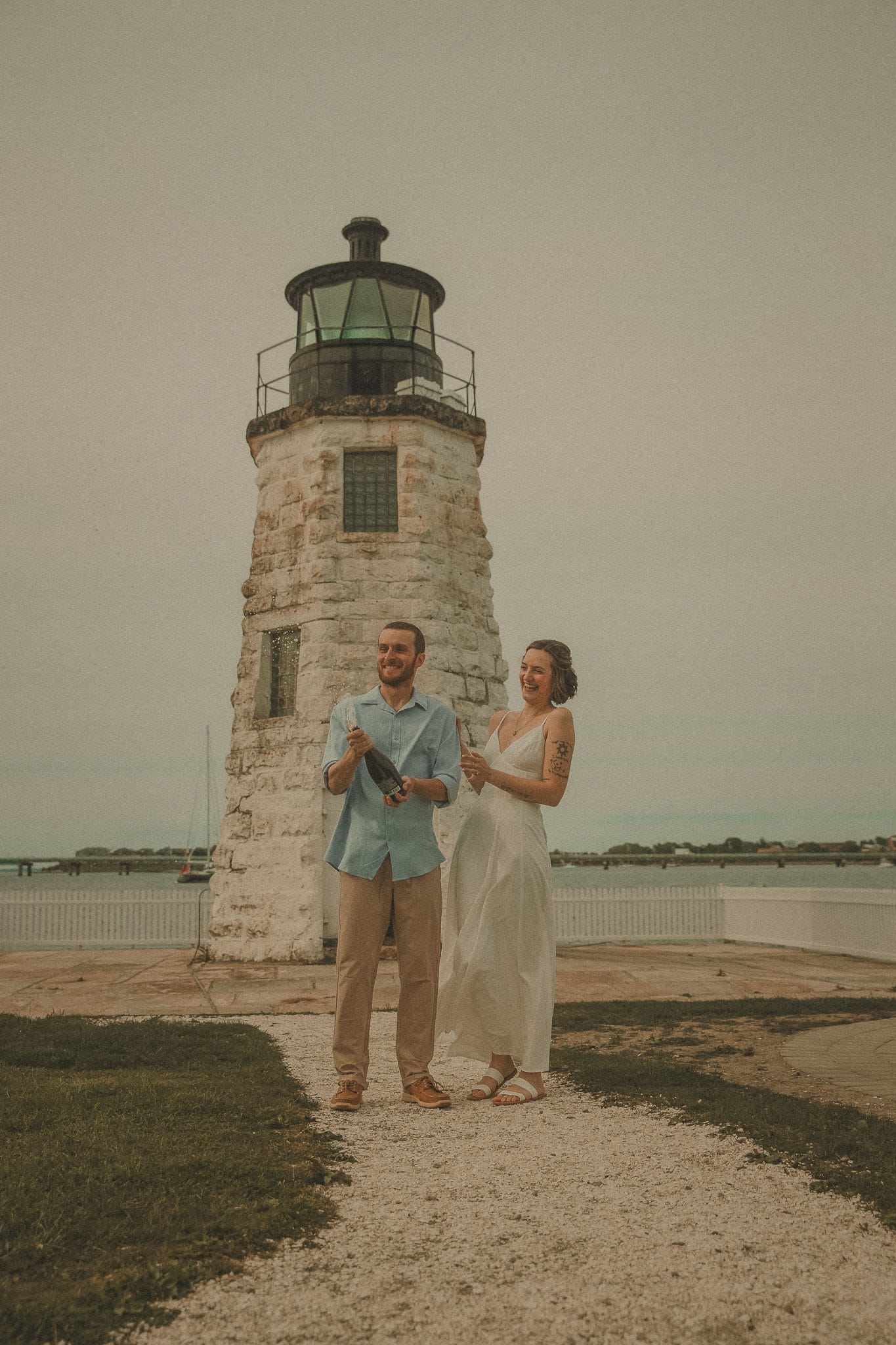 Couple laughing and popping champagne in front of Goat Island Lighthouse with waterfront views in the background