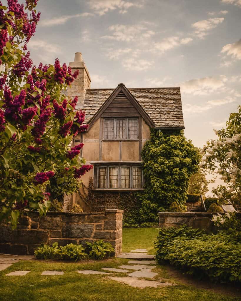 Chase Cottage at Topsmead State Forest in Litchfield, CT, framed by blooming purple lilacs and a stone garden path in spring