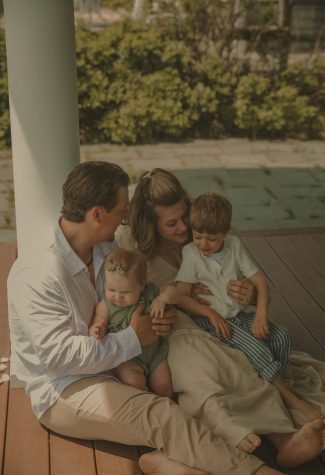 Connecticut family photographer captures parents with toddler and baby sharing a tender moment on a beachside porch at golden hour