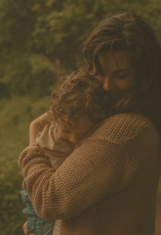 Connecticut family photographer captures a mother in a warm knit sweater holding her young child in a close embrace against a soft woodland backdrop