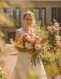Connecticut wedding photographer captures bride smiling in dappled sunlight holding a lush wildflower bouquet in an outdoor garden setting
