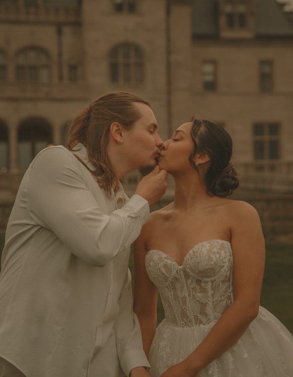 Connecticut wedding photographer captures bride and groom sharing a tender kiss while holding hands in front of a grand historic mansion