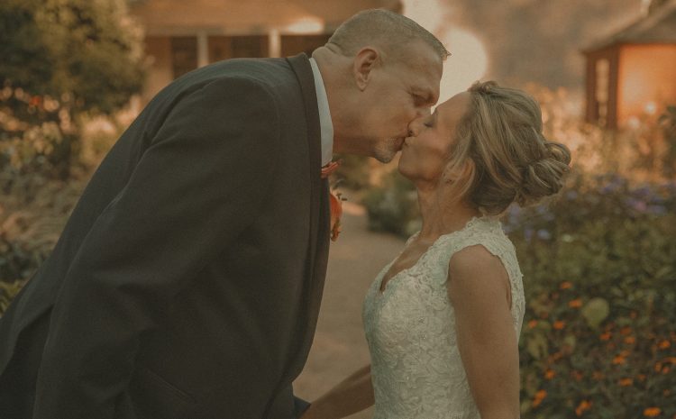 Connecticut wedding photographer captures bride and groom sharing a first kiss in a garden setting bathed in warm amber golden hour light