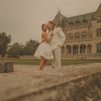 Connecticut wedding photographer captures groom kissing bride on the cheek as she looks toward the camera in front of a grand stone mansion