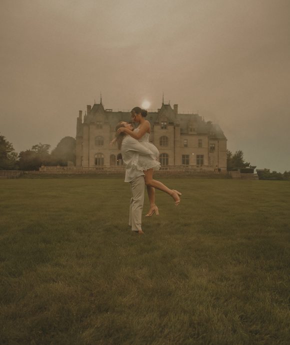 Connecticut wedding photographer captures groom lifting bride on the lawn of a dramatic historic estate under a moody evening sky