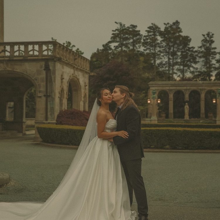 Connecticut wedding photographer captures bride and groom sharing a tender kiss on the grounds of a grand stone estate at dusk